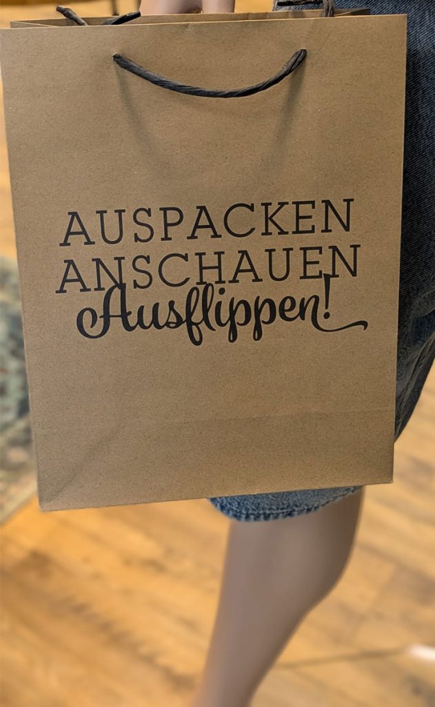 Einkaufstasche im Jeans House Olching mit dem Schriftzug „Auspacken Anschauen Ausflippen“.