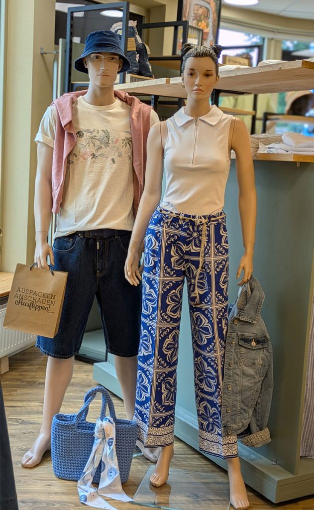 Sommerkollektion 2026 im Jeans House Olching mit weißem Polotop, gemusterter Hose, Bucket Hat und Denim-Shorts.